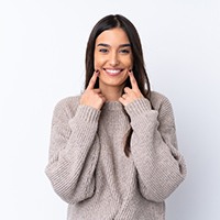 Woman in brown sweater pointing to her smile with two fingers