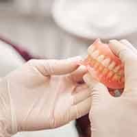 White-gloved hands holding a full set of dentures