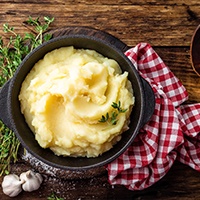 Bowl of mashed potatoes on table next to napkin and wooden spoon
