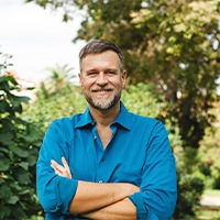 Senior man in collared shirt smiling outside with arms folded